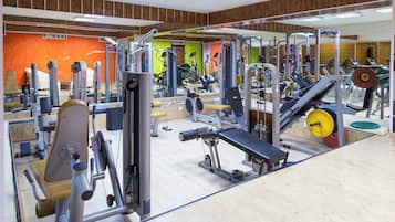 A gym with various exercise equipment, including weight machines and free weights, and a mirrored wall.