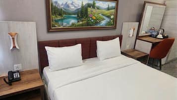 Habitación de hotel con cama, escritorio, silla, teléfono y un cuadro de un paisaje.