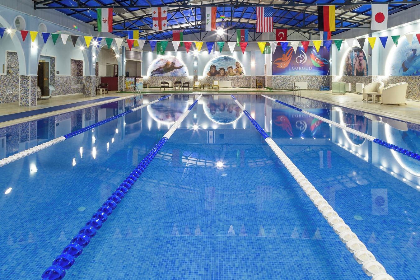 Una piscina interior con carriles delimitados, rodeada de paredes decoradas con banderas e insignias internacionales.