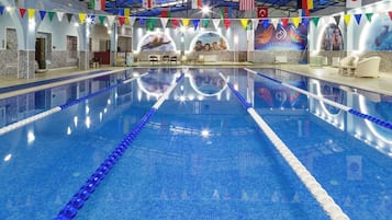 Una piscina interior con carriles delimitados, rodeada de paredes decoradas con banderas e insignias internacionales.