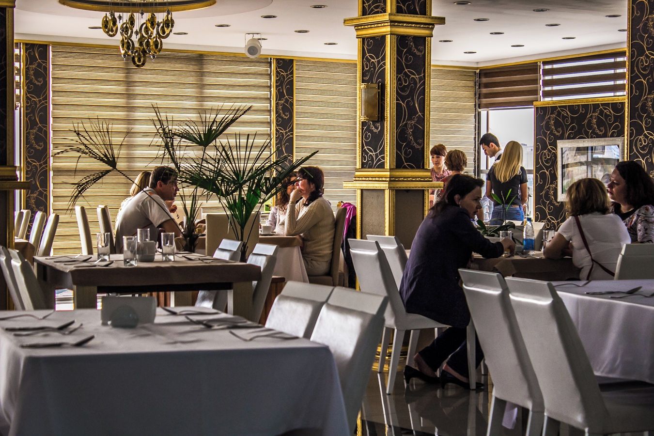 A restaurant with tables set for dining, a chandelier, and decorative wall panels.