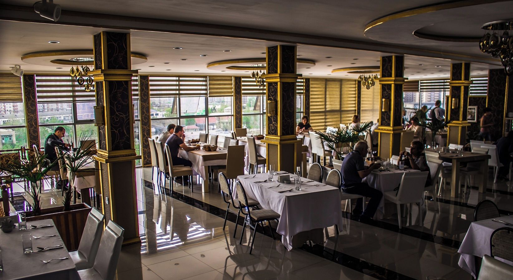 Un restaurant spacieux, doté de nombreuses tables, de chaises et offrant une vue sur la ville grâce à de grandes fenêtres.