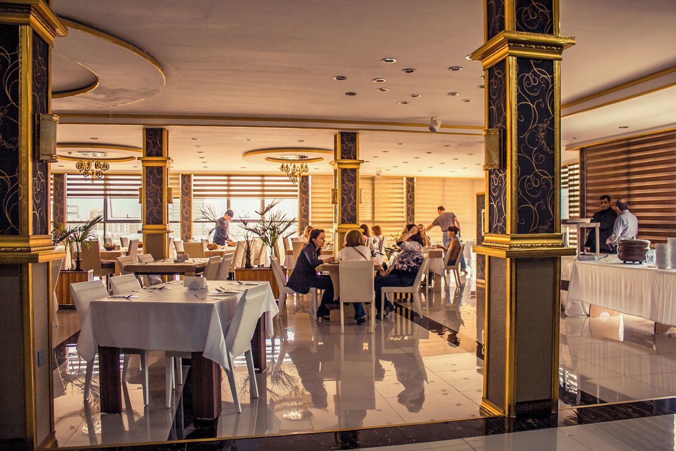 A spacious dining area with multiple tables and chairs, large windows, and elegant architectural details.
