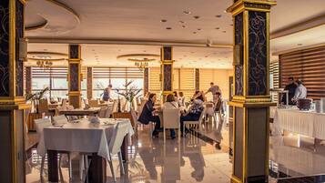 A spacious dining area with multiple tables and chairs, large windows, and elegant architectural details.