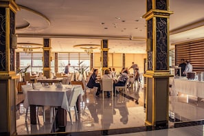 Un comedor amplio con varias mesas y sillas, ventanas grandes y detalles arquitectónicos elegantes.