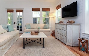 A living room with a white sofa, a white coffee table, a white dresser, and a television mounted on the wall. - Southern Charm | Bikes & Private Beach (Santa Rosa Beach)
