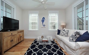 A living room with a television, a white sofa, patterned cushions, a coffee table, and a decorative seahorse painting. - Southern Charm | Bikes & Private Beach (Santa Rosa Beach)
