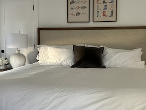 Ein Hotelzimmer mit einem großen Bett, weißer Bettwäsche, einem Nachttisch mit Lampe und zwei gerahmten Bildern an der Wand.