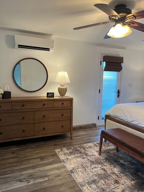 Un dormitorio con un aparador de madera, un espejo redondo, una lámpara de noche, una cama con cabecera y un ventilador de techo.