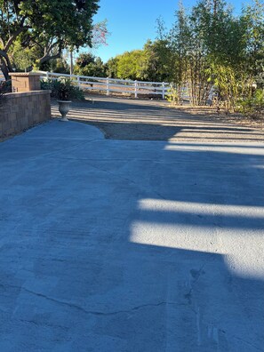 A paved area with a white fence, trees, and a stone planter. - Beautiful 1 bed 1 bath 769sq ft upgraded Casita near downtown Fallbrook ! (Fallbrook)