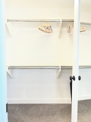 A room with a white wall, a metal rack with hangers, a door with a black handle, and a textured carpet. - Beautiful 1 bed 1 bath 769sq ft upgraded Casita near downtown Fallbrook ! (Fallbrook)