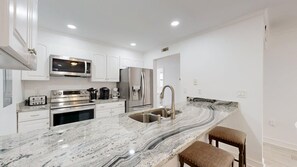 A modern kitchen with white cabinetry, stainless steel appliances, a marble countertop, and a built-in sink. - 89 The Moorings: 2  BR, 3  BA Villa in Hilton Head, Sleeps 6 (Hilton Head)