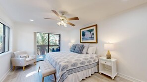 A bedroom with a bed, a chair, a bedside table, a ceiling fan, and a window with a view of palm trees. - 89 The Moorings: 2  BR, 3  BA Villa in Hilton Head, Sleeps 6 (Hilton Head)