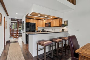 A modern kitchen with wooden cabinets, a built-in island with bar stools, and a staircase leading to another level. - New! FOREteener’s Retreat | AC, Pool, Hot Tub, Golf & Ski (Durango)