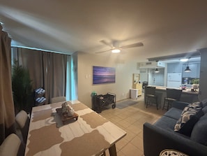 A living room with a dining table, a sofa, a ceiling fan, and a kitchen area with a refrigerator and cabinets. - Cozy 1-bedroom condo in tranquil South Padre Island with Pool View ,beach access (South Padre Island)