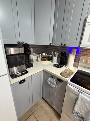 A kitchen with grey cabinets, a coffee maker, a toaster, and a stove. - Cozy 1-bedroom condo in tranquil South Padre Island with Pool View ,beach access (South Padre Island)