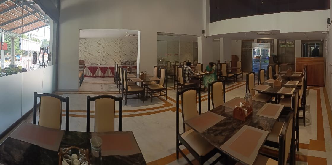 Un restaurante amplio con varias mesas y sillas, una pared de mármol y vistas al exterior.