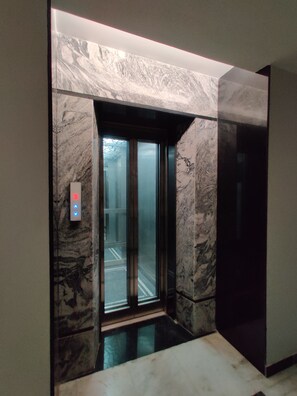 Un ascensor con pared de mármol y panel de control con botones iluminados.