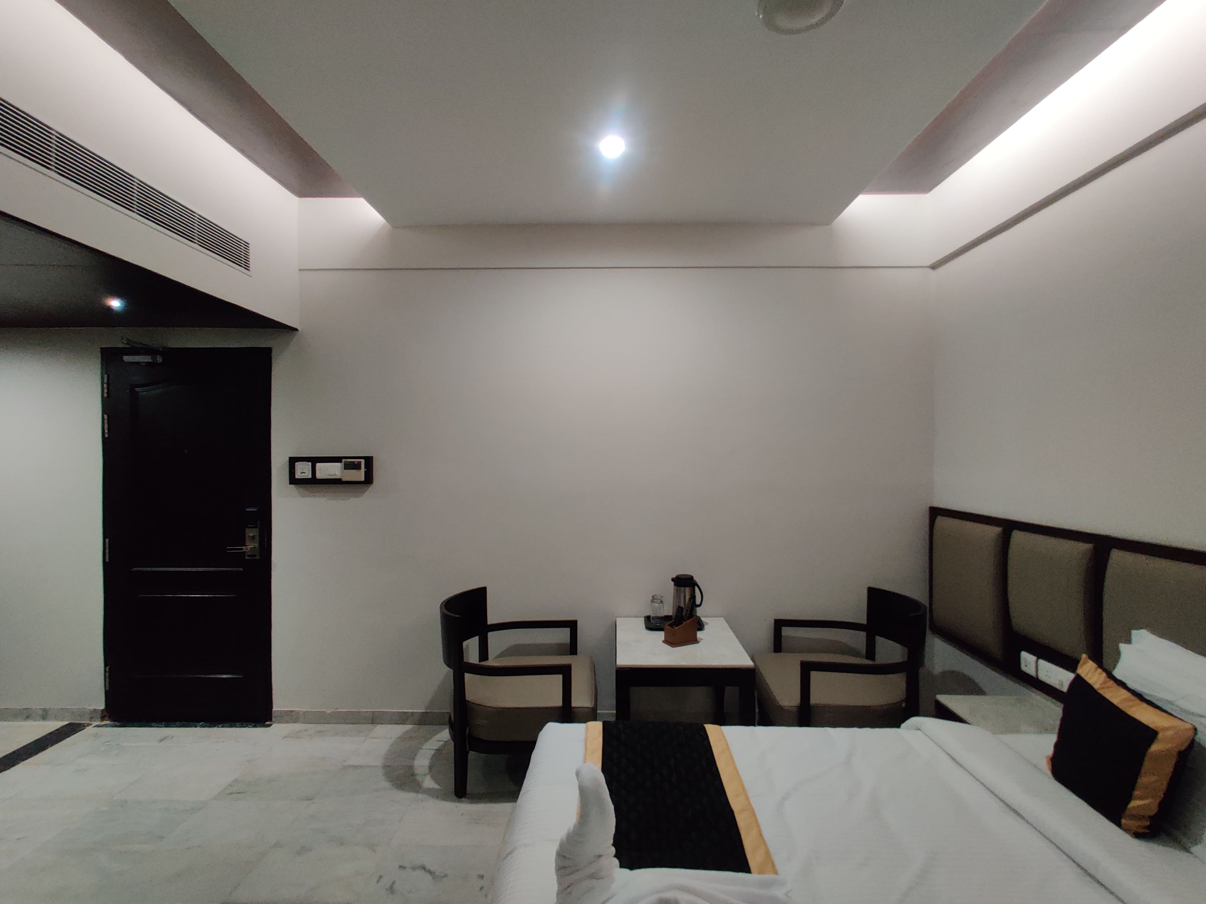 A hotel room with a bed, two chairs, a small table, and a door.