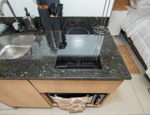 A kitchen with a built-in induction cooktop, a sink, and a wooden cabinet below. - Corporate Stays First del Sol - 604 (Asunción)