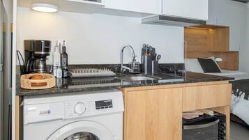 Una cocina compacta con lavadora integrada, microondas y cafetera.