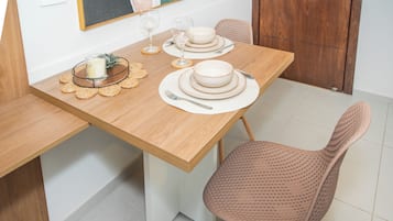 Una mesa de comedor dispuesta con platos, tazones, cubiertos y una vela, con una silla y un interruptor de luz en la pared.