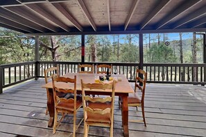 A wooden deck with a table and chairs, surrounded by a railing, overlooking a forested area. - Gonzo Chalet | Spacious Deck + Mountain Views (Ruidoso)
