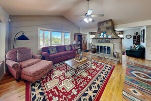 A living room with a fireplace, a sofa, a patterned armchair, and a large rug. - Gonzo Chalet | Spacious Deck + Mountain Views (Ruidoso)