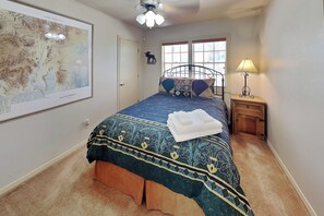 A bedroom with a bed, a nightstand, a lamp, a map on the wall, and a window with blinds. - Gonzo Chalet | Spacious Deck + Mountain Views (Ruidoso)