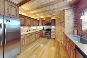 A modern kitchen with wooden cabinets, stainless steel appliances, and a wooden floor. - Twin Bears | Fireplace, Pool Table, & Mountain Views (Ruidoso)