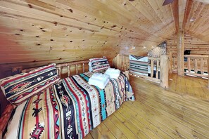A wooden cabin interior with a bed, pillows, and a stone wall. - Twin Bears | Fireplace, Pool Table, & Mountain Views (Ruidoso)
