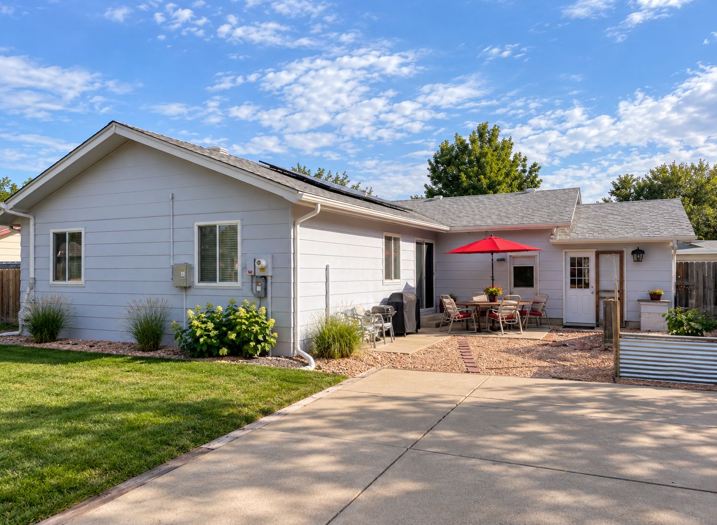 A single-story house with a patio area, a covered grill, and a red umbrella.