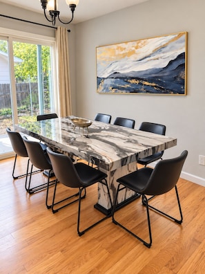 Uma sala de jantar com mesa de mármore, cadeiras pretas e um quadro na parede.