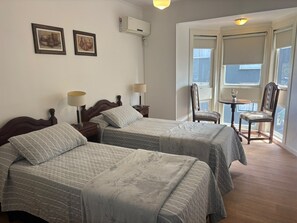 A hotel room with two beds, a small table, chairs, and a window with a view. - Bakumare Hotel (Pinamar)