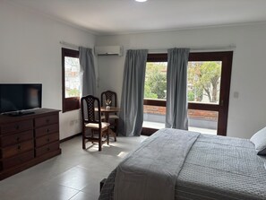 A hotel room with a bed, a TV on a dresser, a dining table with chairs, and a balcony with curtains. - Bakumare Hotel (Pinamar)