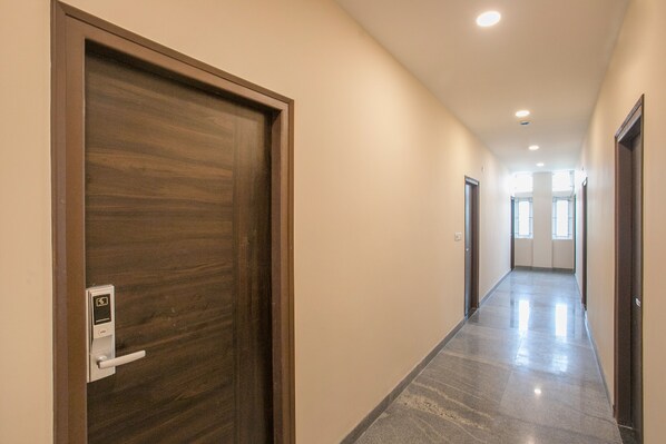 Um corredor com porta de madeira à esquerda, um interruptor de luz e uma porta à direita.