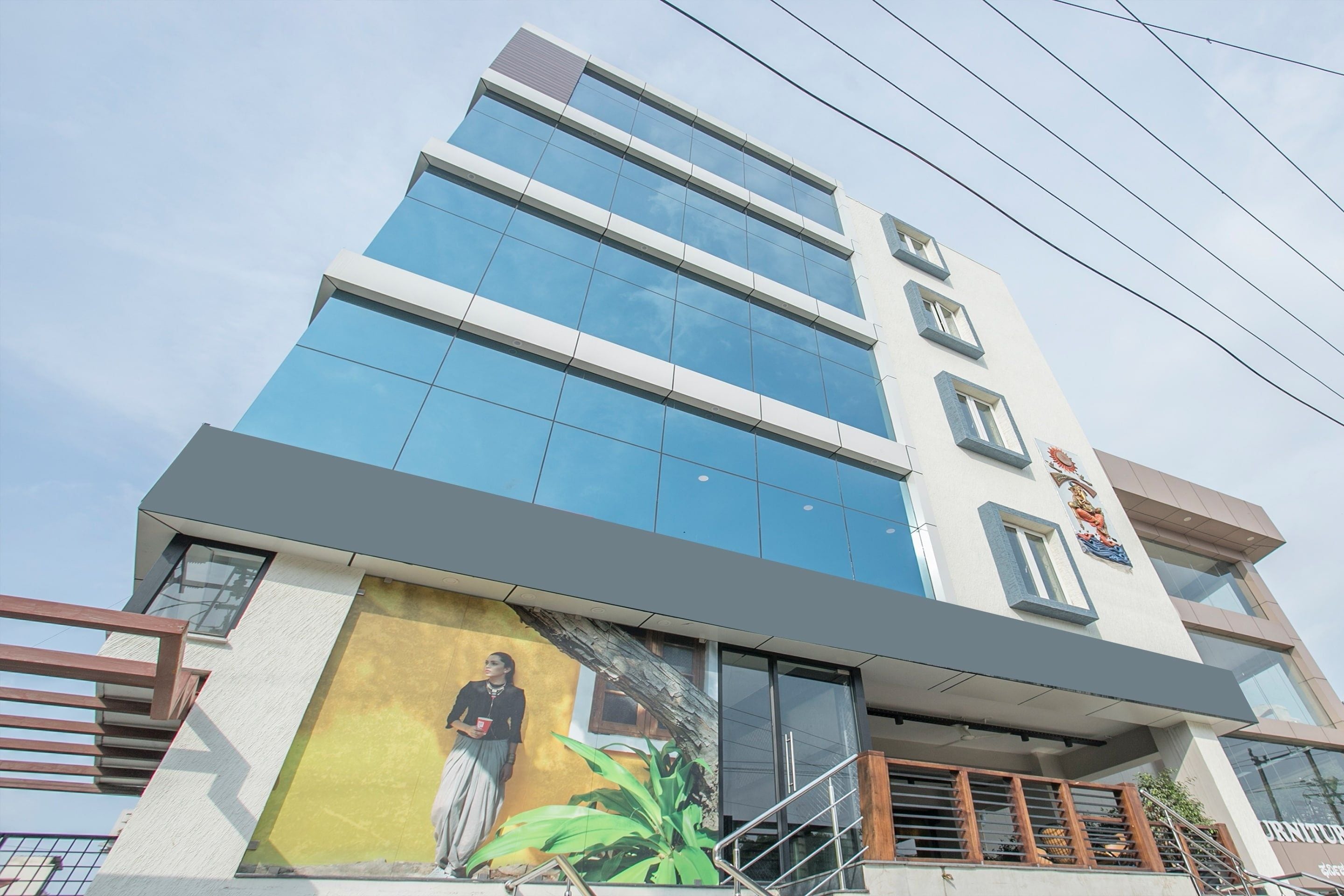 Un edificio moderno con fachada de vidrio, un mural en la parte baja y una escalera que lleva a la entrada.