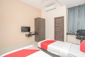 Quarto de hotel com duas camas, televisão, guarda-roupa, secretária e janela com cortinas.