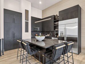 A modern kitchen with dark cabinetry, a stainless steel refrigerator, a marble countertop, and bar stools. - Ski-In/Out Luxury | Private Hot Tub + Sauna (Brian Head)