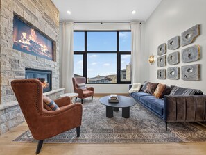 A modern living room with a fireplace, large windows, and a view of the outside. - Ski-In/Out Luxury | Private Hot Tub + Sauna (Brian Head)