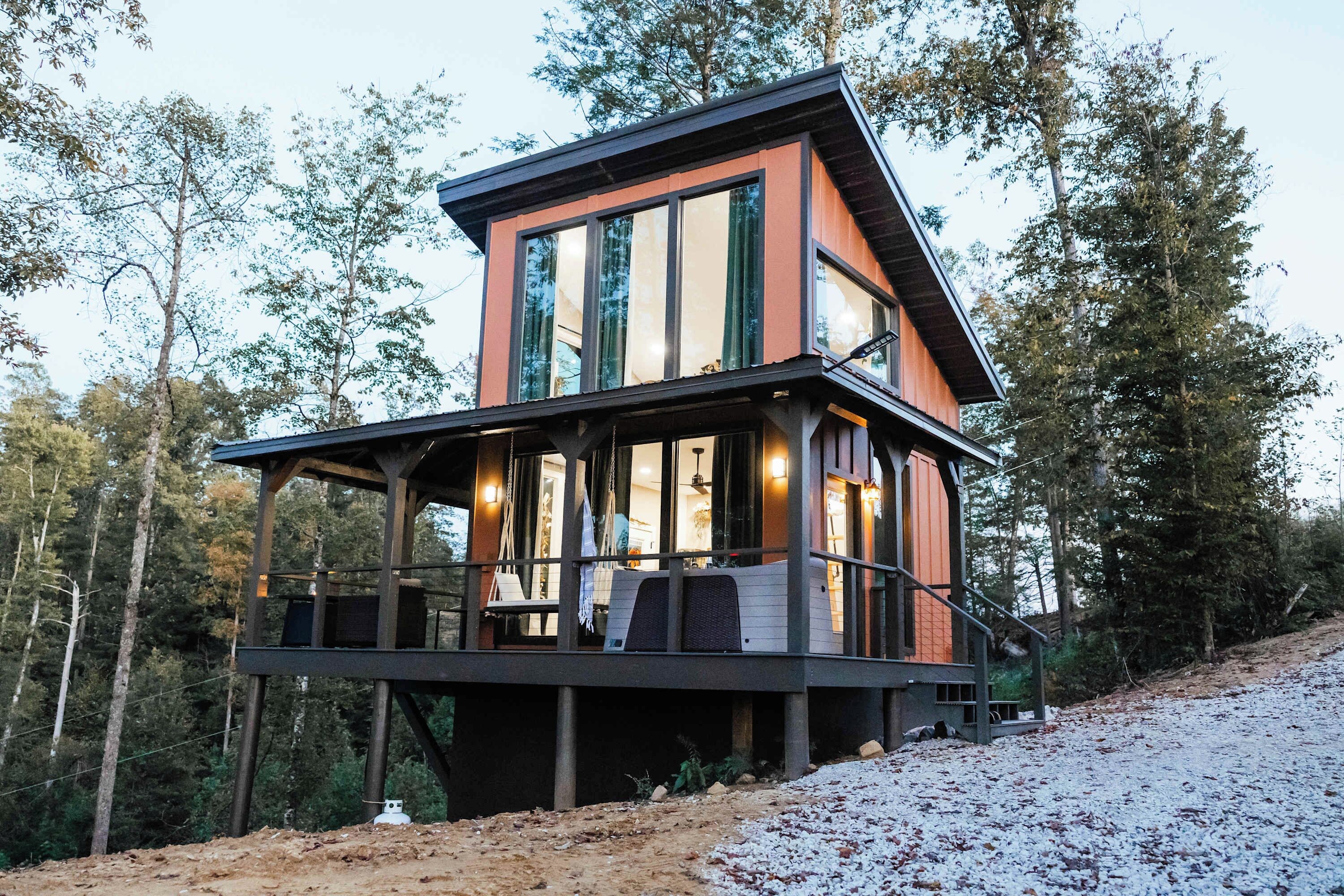 A multi-level wooden cabin with large windows, a balcony, and a staircase leading to the upper level.