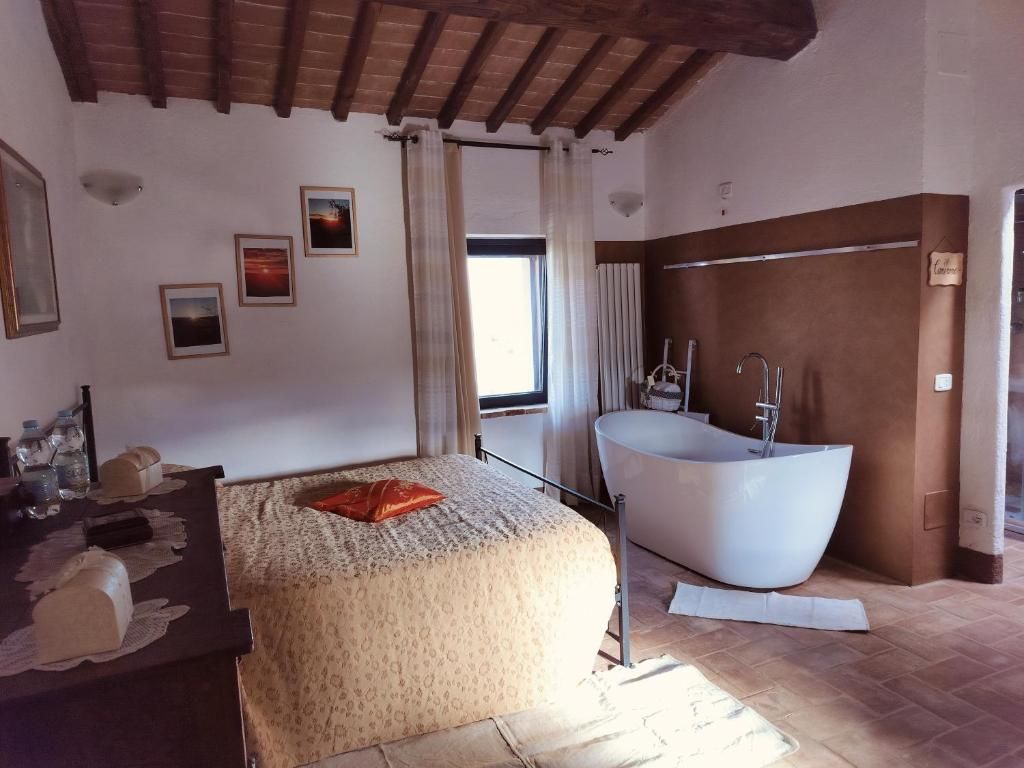 A bedroom with a bed, a large window, a bathtub, and a wooden ceiling.