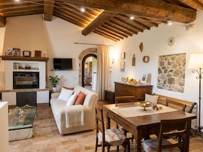 A cozy living room with a fireplace, a television, and a dining area with a wooden table and chairs. - Vecchio Casale Quercetino  (Montenero)