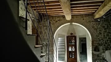 Habitación con paredes de piedra, una escalera de madera y una puerta que da a otra estancia.