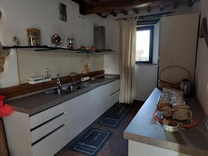 A kitchen with a sink, cabinets, and a window. There are shelves with jars and a kettle.