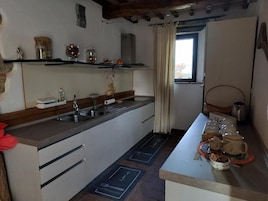 Una cocina con lavamanos, armarios y ventana. Se observan estantes con frascos y una tetera.