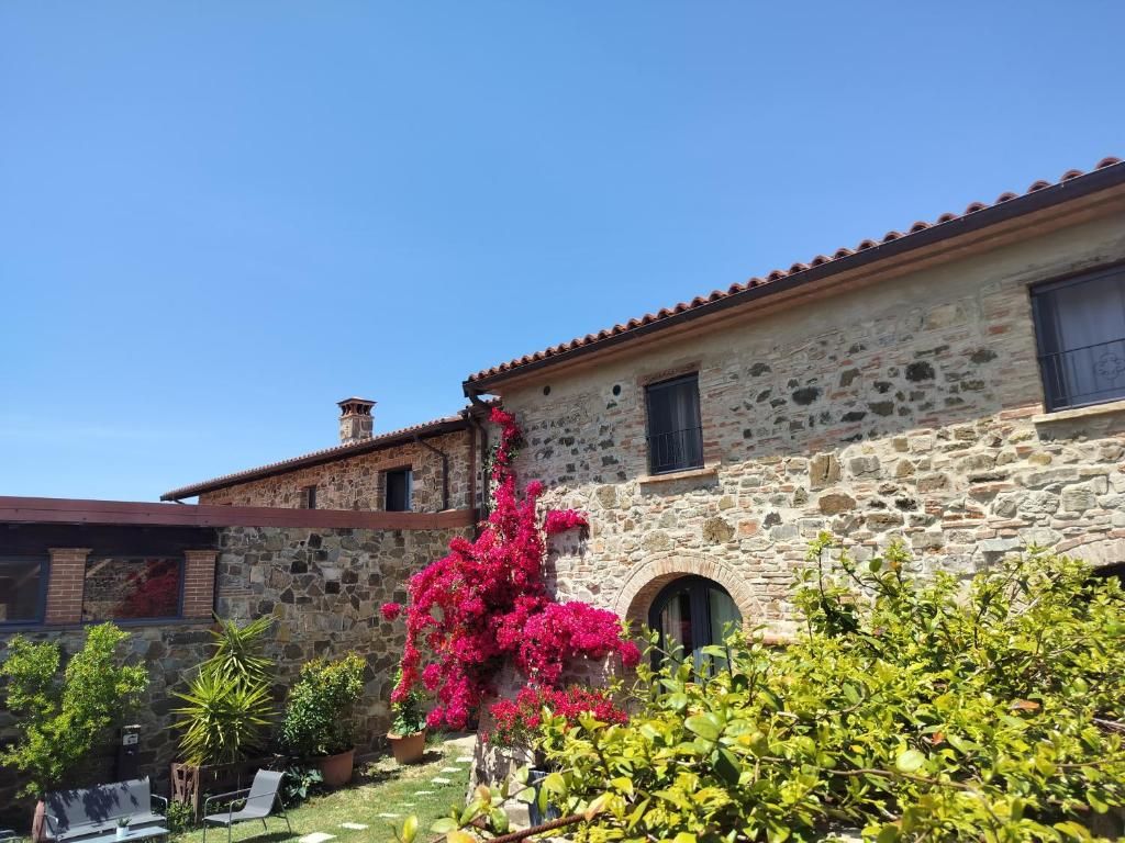 A stone building with a tiled roof, a small tower, and a garden with flowering plants.