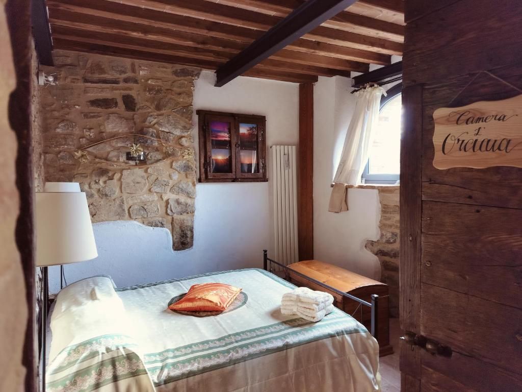 Een rustieke slaapkamer met een stenen muur, houten balken, een bed met een groen-witte dekbedovertrek, een nachtkastje en een raam met gordijn.