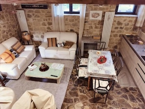 A cozy living room with a stone wall, a white sofa, a coffee table, and a dining table with chairs. - Vecchio Casale Quercetino  (Montenero)
