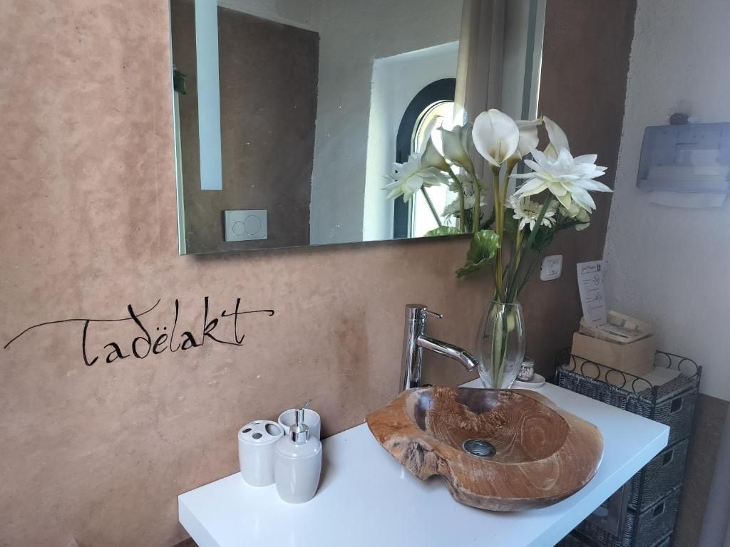 Une salle de bain avec un lavabo blanc, un miroir et un vase contenant des fleurs blanches.